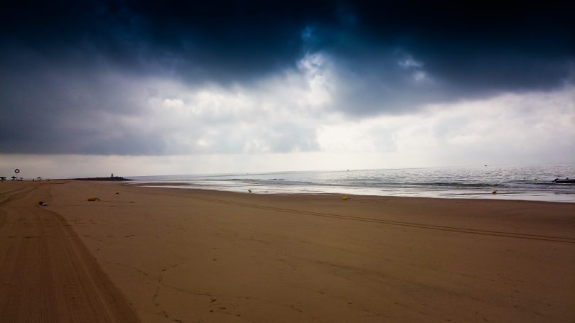 Düsterer Strand mit sanften Wellen und bewölktem Himmel im Hintergrund.